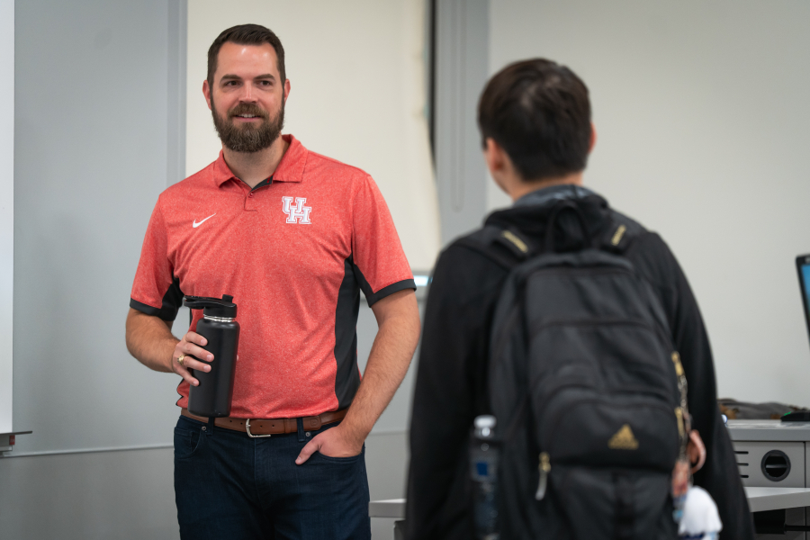 Zelisko, left, speaks with a student, right, against a grey and white background. Zelisko faces the camera while the student faces away.