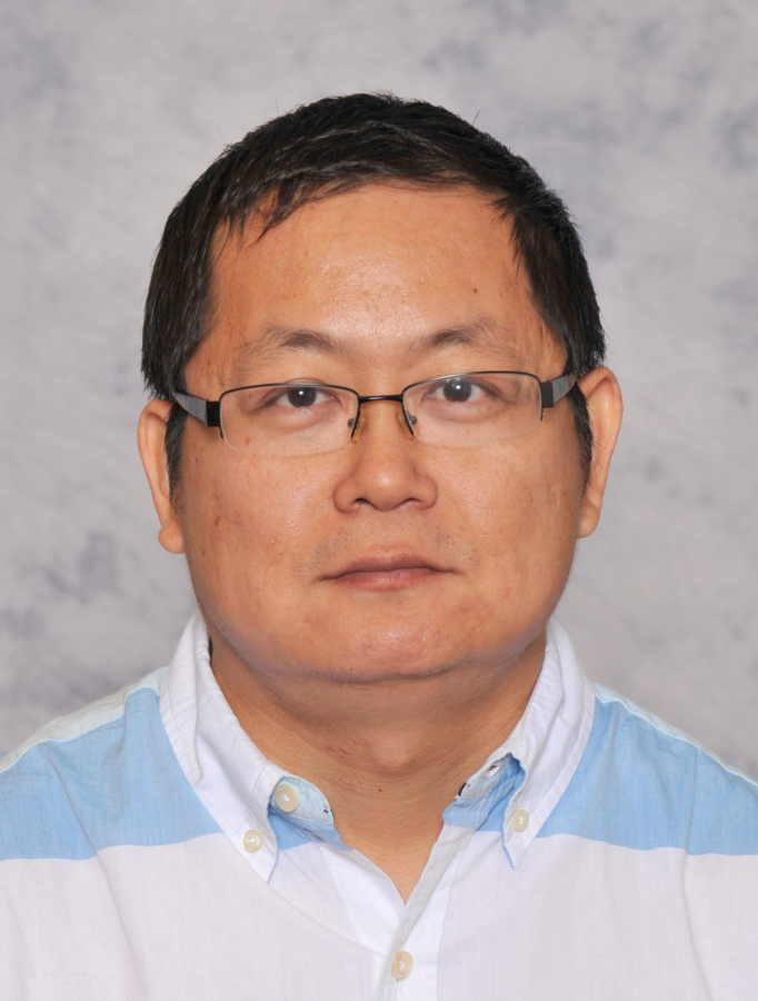 Weihang Zhu wears a blue and white collared shirt against a grey background in this headshot. He has short, dark hair, and is wearing glasses.