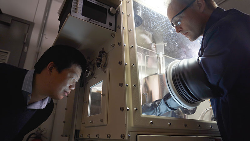 Yan Yao watches as student Benjamin J. Emley works in a glovebox.