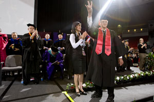 John Rogers stops on stage and flashes a Cougar sign before a packed house at spring commencement Saturday. Photo by Thomas Shea.