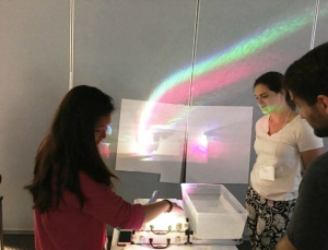 Gwen Musial, (second from right) watches as students use a prism to split white light into a rainbow