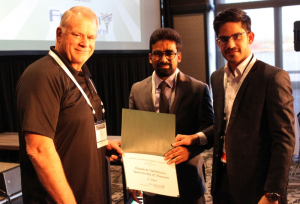 FlexSim CEO Bill Nordgren presents an award to University of Houston graduate students Muhammad Zia-ul-Haq Hussain and Moaz Ahmed for their third place finish at the annual Healthcare Systems Process Improvement Conference.